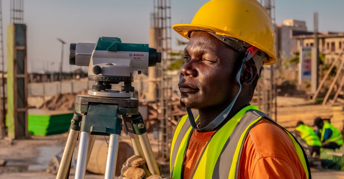 A construction worker using a theodolite for land surveying at a building site.